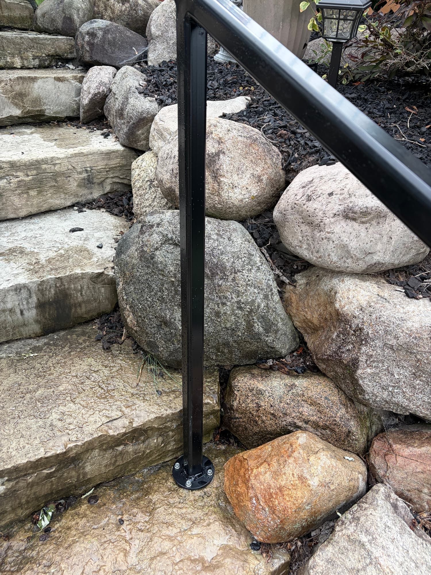 Close view of a handrail post bolted to a stone step through a round steel base plate
