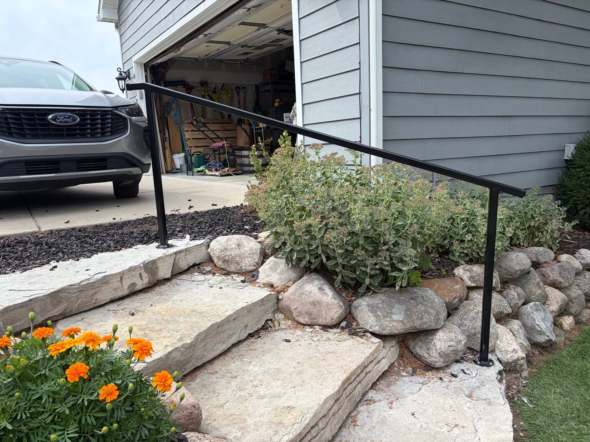 Second black steel handrail alongside a short natural-stone entry walk beside a driveway